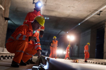 Male construction workers examining underground tracks at dark underground construction site