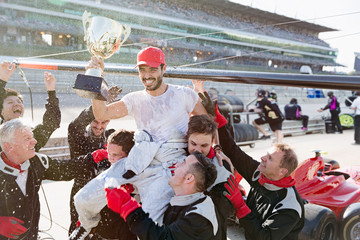Formula one racing team carrying driver trophy on shoulders, celebrating victory on sports track