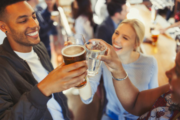Enthusiastic friends toasting beer and wine glasses at bar