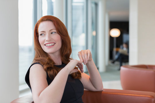 Smiling businesswoman with red hair looking over shoulder in lounge