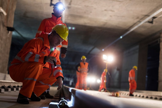 Male construction workers examining underground tracks at dark underground construction site