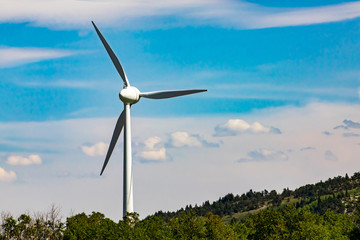 A single wind turbine is seen in rural Alberta, Canada. Against a blue sky with scattered clouds....