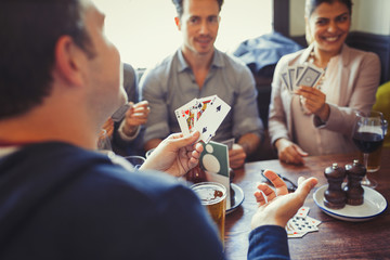 Friends playing poker and drinking beer and wine at table in bar