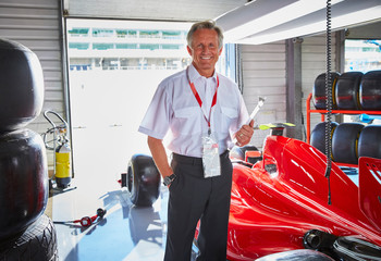 Portrait confident formula one manager next to race car in repair garage