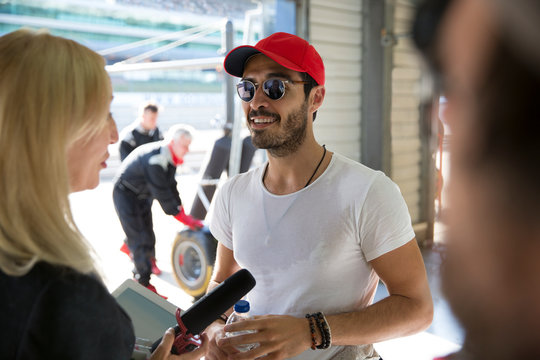 Female news reporter interviewing male race formula one driver in repair garage