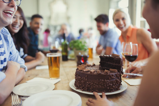 Woman serving chocolate birthday cake to friends at restaurant table