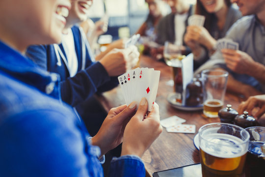 Woman holding aces four of a kind, playing poker drinking beer friends at table in bar