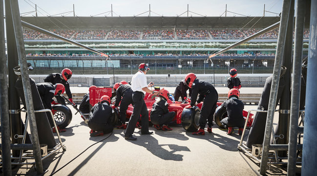 Manager pit crew replacing tires on formula one race car in pit lane