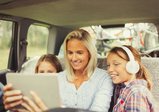 Mother daughters watching video on digital tablet in back seat of car