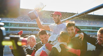 Formula one racing team carrying driver trophy on shoulders, celebrating victory