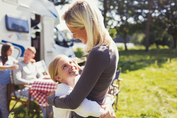 Affectionate mother and daughter hugging outside sunny motor home
