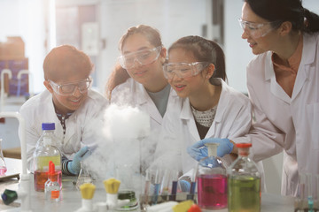 Female teacher and students watching scientific experiment chemical reaction in laboratory classroom