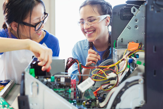 Smiling girl students assembling computer in classroom