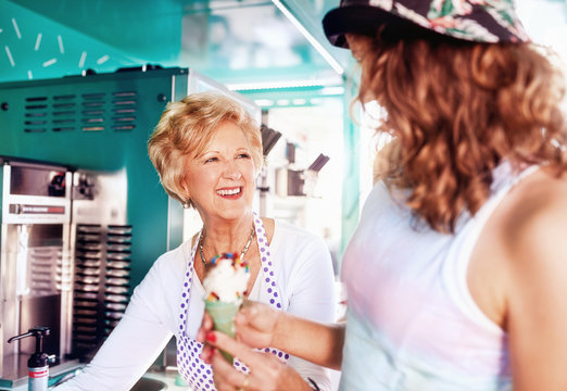 Smiling senior female business owner serving ice cream to young woman at food cart