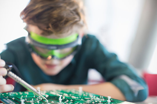Focused boy student soldering circuit board in classroom