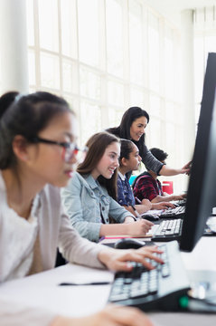 Female teacher helping students working at computers in computer lab classroom