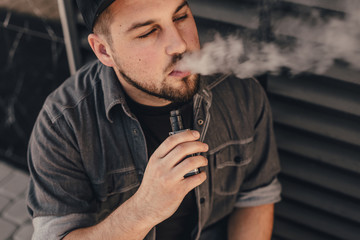 Young handsome man smoke with vape near black wall