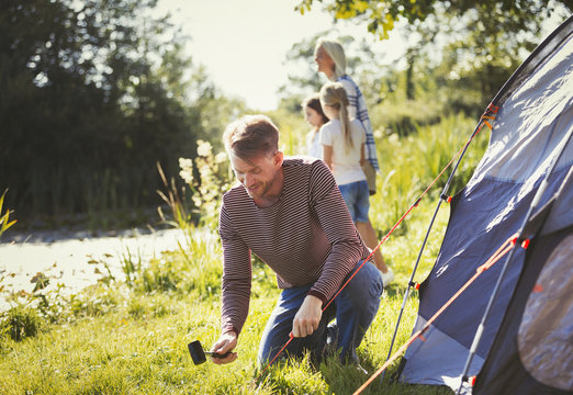 Father pitching tent at sunny lakeside campsite