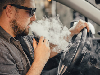 Young handsome man smoke with vape in vehicle