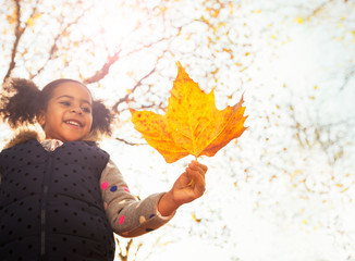 Smiling girl holding orange maple leaf in sunny autumn park