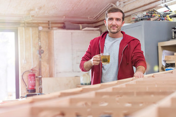 Portrait confident male carpenter drinking tea at wood boat in workshop