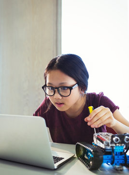 Focused, curious girl programming assembling robotics at laptop in classroom