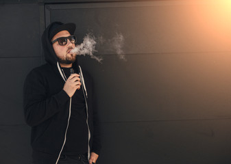 Young handsome man smoke with vape near black wall