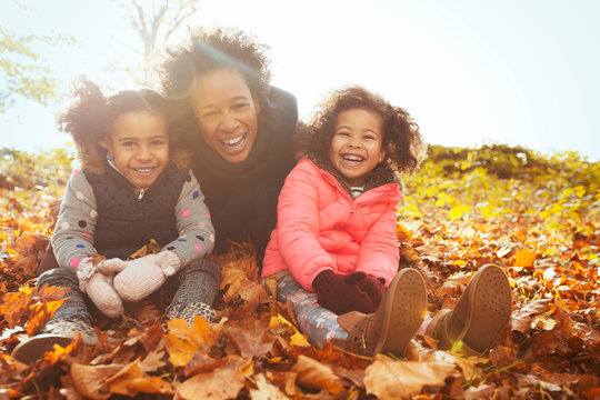 Portrait playful mother and daughters in autumn leaves in sunny park