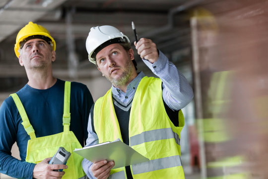 Male foreman engineer with clipboard looking up at construction site