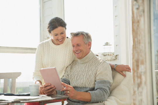 Smiling mature couple using digital tablet at table on sunny sun porch