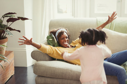Enthusiastic mother on sofa greeting running daughter