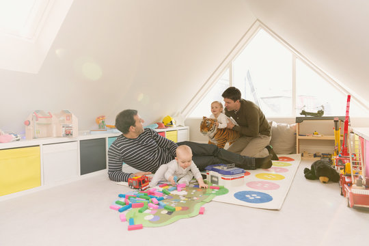 Male gay parents playing with baby sons in playroom