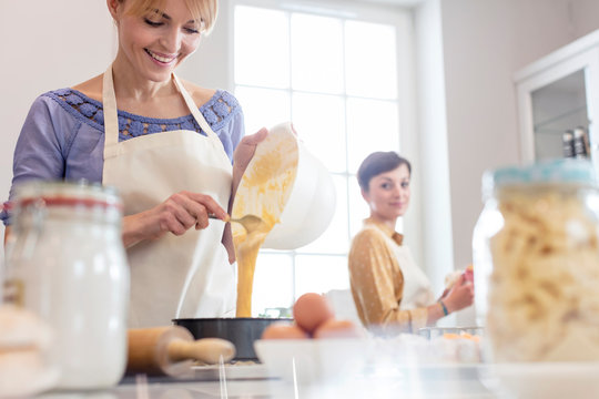 Female caterers baking, pouring cake batter into tin in kitchen