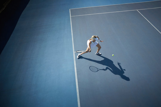Overhead view young female tennis player playing tennis, hitting the ball on sunny blue tennis court