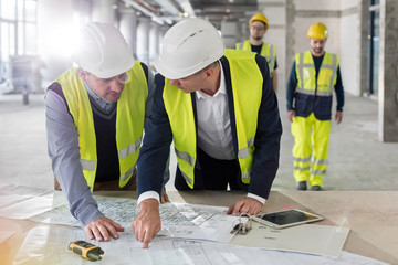 Male engineers discussing blueprints at construction site