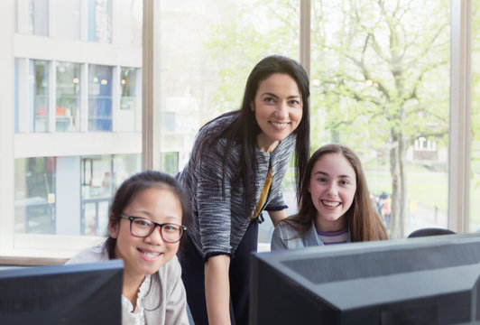 Portrait confident, smiling female teacher girl students researching at computer in library