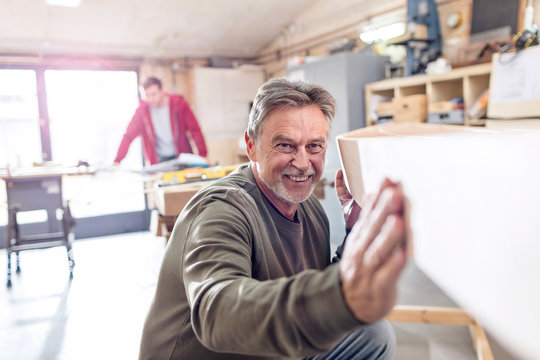 Smiling male carpenter examining wood boat in workshop