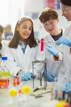 Curious students conducting scientific experiment, watching liquid in vial in laboratory classroom