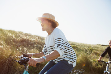 Playful mature woman riding bicycle on sunny beach grass path
