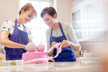 Female caterers finishing pink wedding cake in kitchen