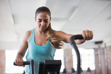 Focused young woman using elliptical trainer in gym
