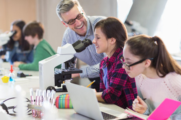 Smiling male science teacher helping girl students conducting scientific experiment at microscope in laboratory