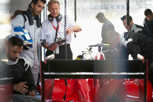 Manager formula one driver watching pit crew working on race car in repair garage