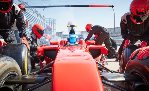 Pit crew replacing tires on formula one race car in pit lane