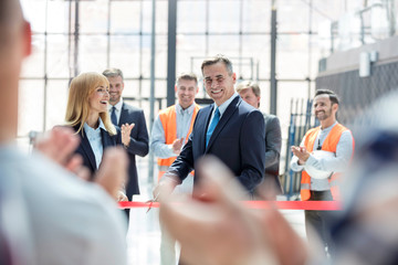 Smiling businessman businesswoman cutting ribbon at new construction site ceremony