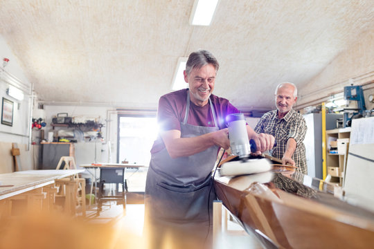 Male carpenters buffing wood boat with sander in workshop