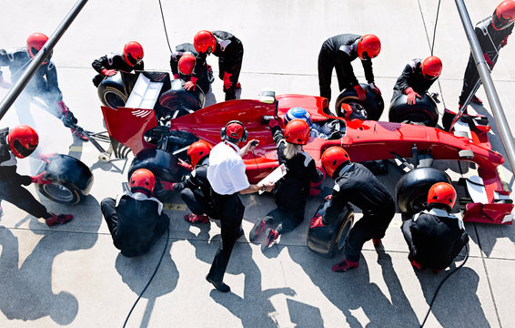 Manager stopwatch timing pit crew replacing tires on formula one race car in pit lane