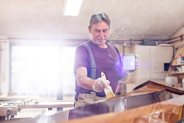 Male carpenter staining wood kayak in workshop