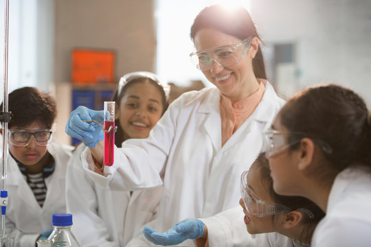 Smiling female chemistry teacher and students conducting scientific experiment in laboratory classroom - Powered by Adobe