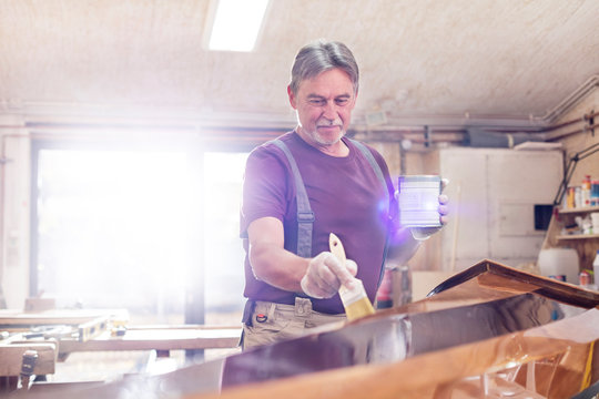 Male Carpenter Staining Wood Kayak In Workshop